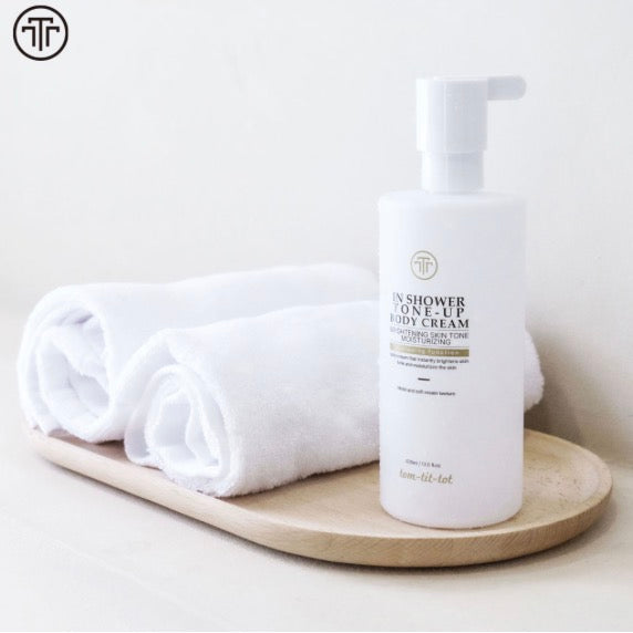 white pump bottle labeled "in shower tone up body cream on wooden tray with white towels