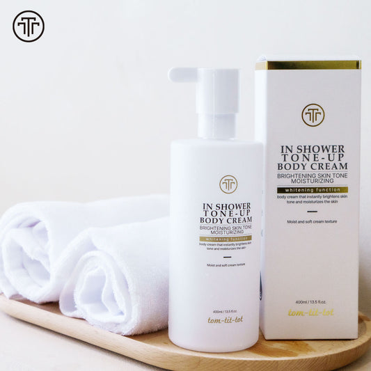 In Shower Tone-Up Body Cream and packaging on a wooden tray with white towels. Reads "brightening skin tone moisturizing"