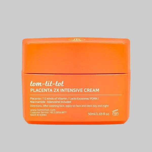 Orange jar of tom-tit-tot Placenta 2X Intensive Cream reading "12 kinds of vitamin, lacto exosome, pdrn, niacinamide" on a gray background